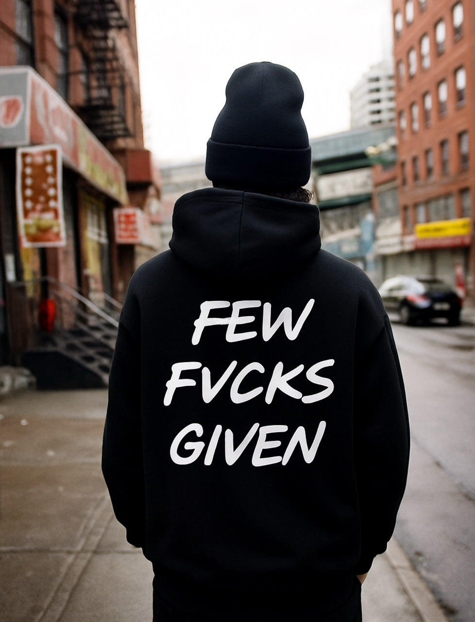 Person wearing a black hoodie with 'FEW FVCKS GIVEN' text on the back in an urban setting. ZERO FUCKS HWY DIV Highway Division