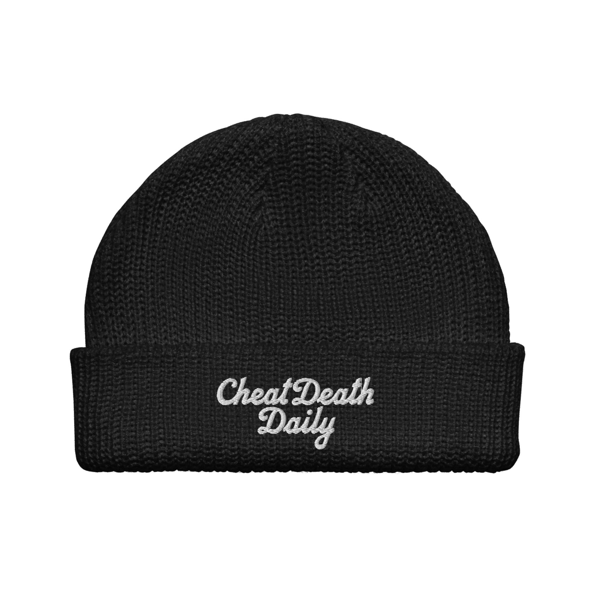 A black fisherman-style beanie from Highway Division is shown, featuring bold white embroidered text on the front cuff that reads “CHEAT DEATH DAILY.” The beanie has a short, cropped fit that sits above the ears in traditional fisherman or dockworker style. Made from soft, stretchable acrylic knit, it offers comfort, warmth, and a snug fit ideal for colder weather or everyday wear. The black fabric provides a clean, minimal base that contrasts sharply with the white stitching, making the embroidered phrase