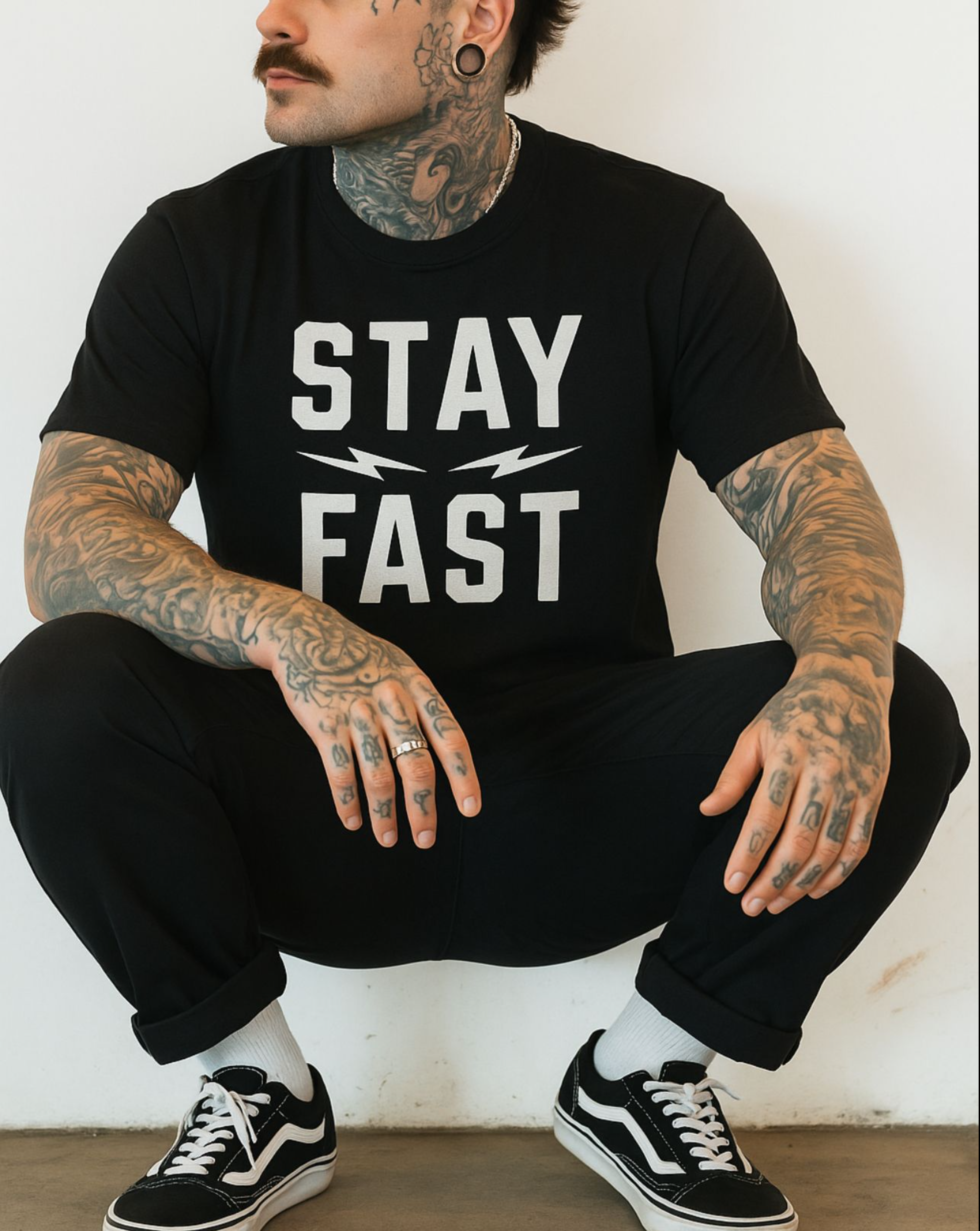 A black short-sleeve t-shirt from Highway Division, displayed flat against a neutral background. The shirt features a bold, minimalist front print in large, capitalized white letters that read “STAY FAST,” centered across the chest. The font is strong and modern, evoking speed and motion, with no other visible graphics, branding, or embellishments on the front or sleeves. The material appears soft and lightweight, likely 100% cotton, with a regular fit and classic crew neckline. There are no visible prints 