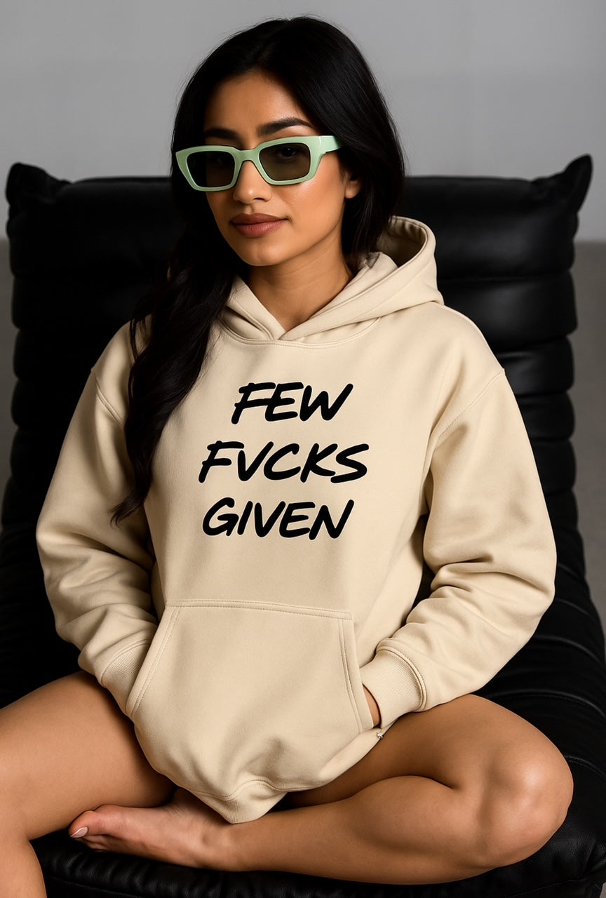 Person wearing a beige hoodie with text sitting on a black chair that reads Few Fucks Given by Highway Division HWY DIV Zero Fucks Given 