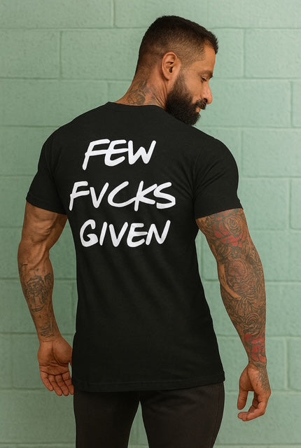 Man wearing a black t-shirt with 'FEW FCKS GIVEN' text on the back against a green brick wall. Zero Fucks Given T Shirt 