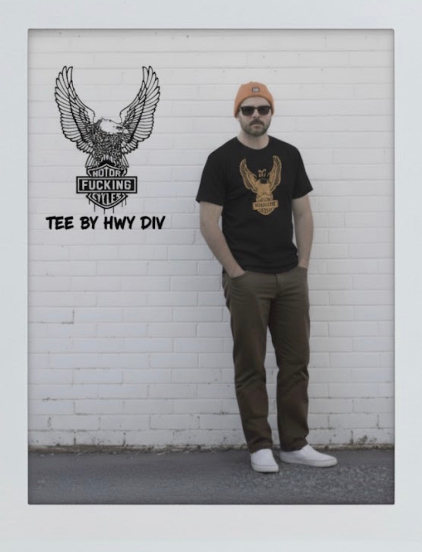 Person wearing a black t-shirt with an eagle design in front of a white brick wall.